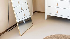 A room with a standing mirror, a dresser with drawers, and a lamp with a feathered shade.