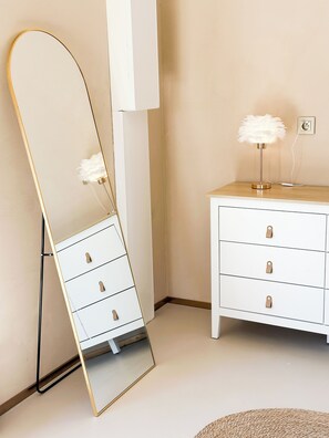 A room with a standing mirror, a dresser with drawers, and a lamp with a feathered shade. - Venus • Private Spa, Jacuzzi & Sauna (L'Arbresle)
