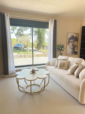 A living room with a sofa, a coffee table, and a view of a car and trees outside.