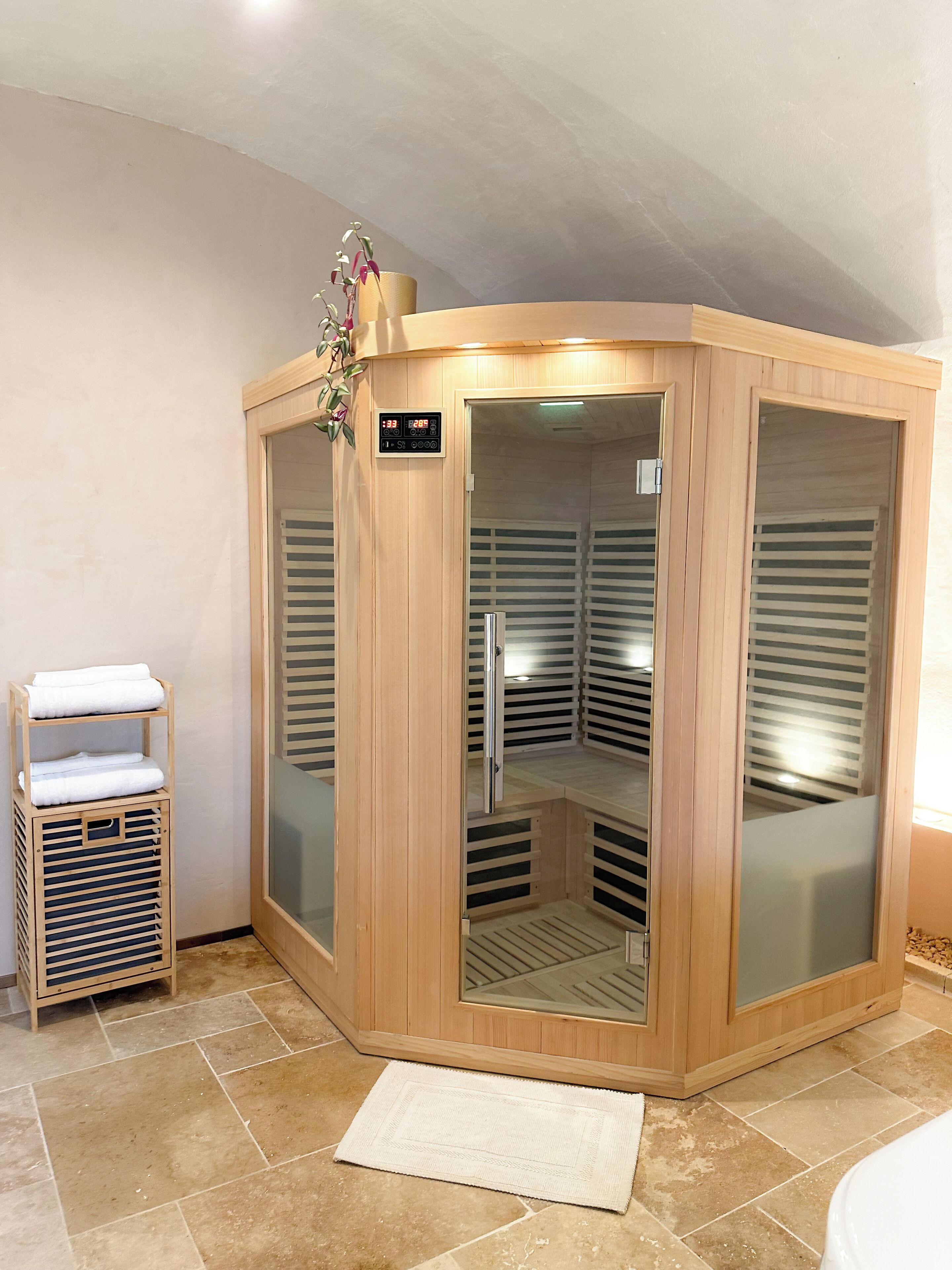 A corner sauna with a wooden exterior, a digital control panel, and a towel rack.