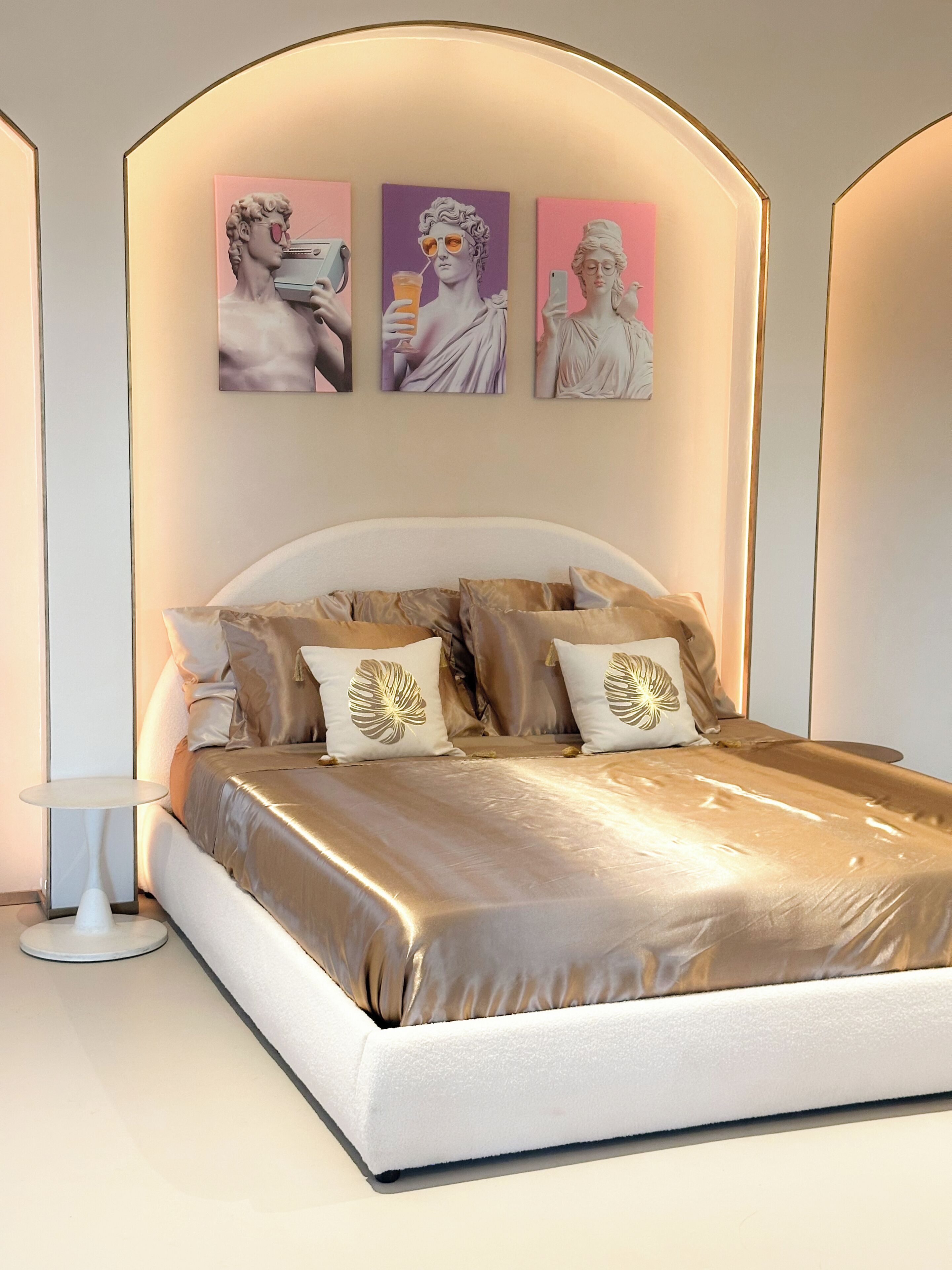 A modern bedroom with a large bed, a bedside table, and three framed artworks on the wall.