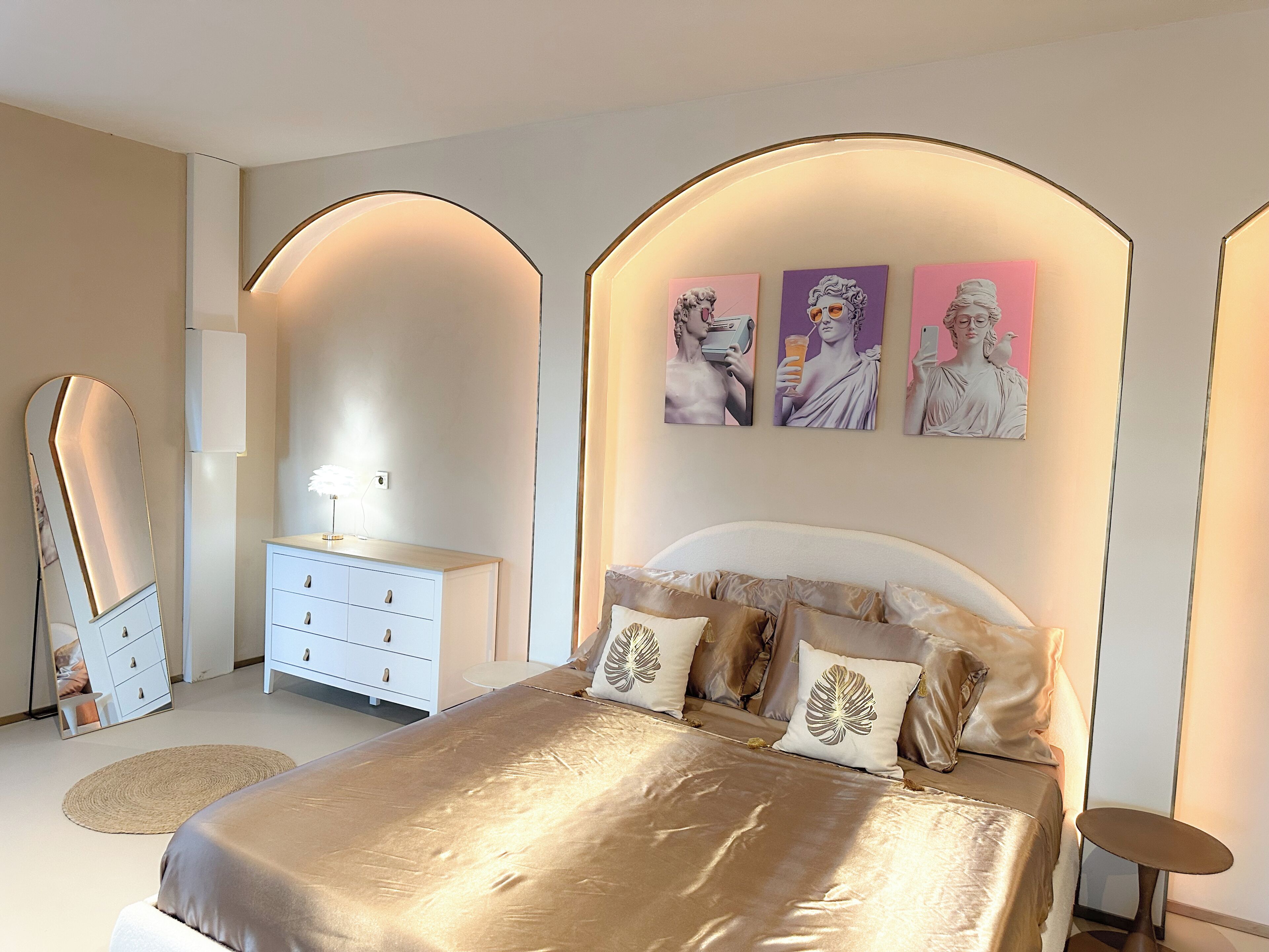 Une chambre à coucher avec un grand lit, une commode, un miroir et des œuvres d’art murales.