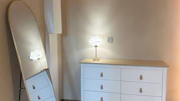 Ein Zimmer mit einem großen Spiegel, einer weißen Kommode mit Schubladen und einer Lampe.