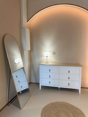 A room with a large mirror, a white dresser with drawers, and a lamp.