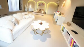 A modern living room with a white sofa, a round coffee table, and a TV on a white stand.