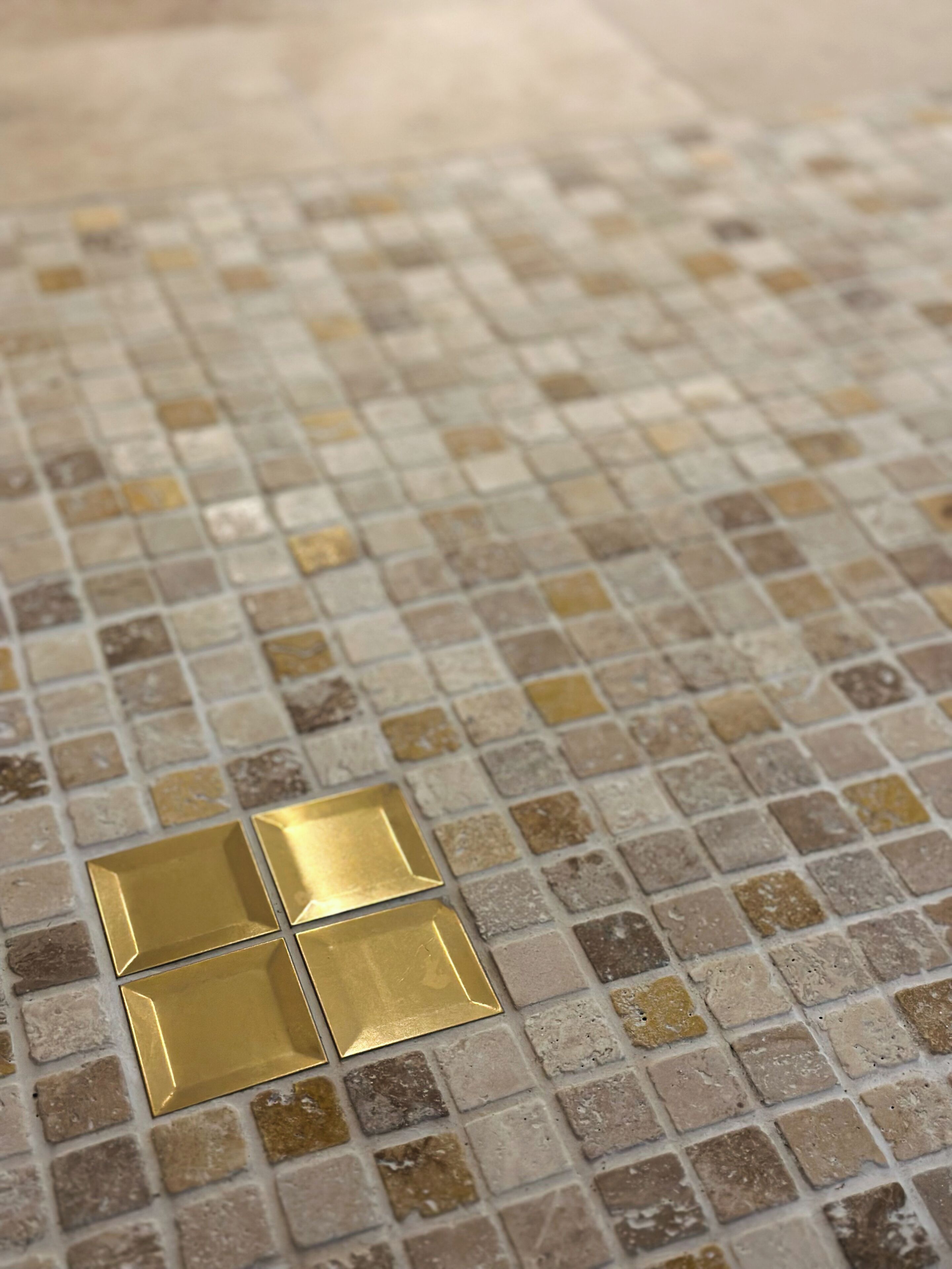 Ein Detailaufnahme eines Fliesenbodens mit einem Muster aus kleinen, quadratischen Fliesen in verschiedenen Beige- und Brauntönen.