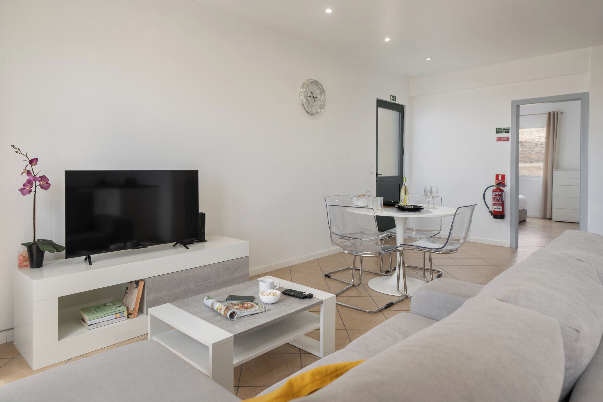 A modern living room with a flat-screen TV, a coffee table, a sofa, and a dining area with chairs.
