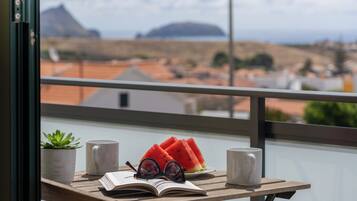 Ein Balkon mit Holztisch, zwei Tassen, einem Buch, einer Brille und einem Blumentopf.