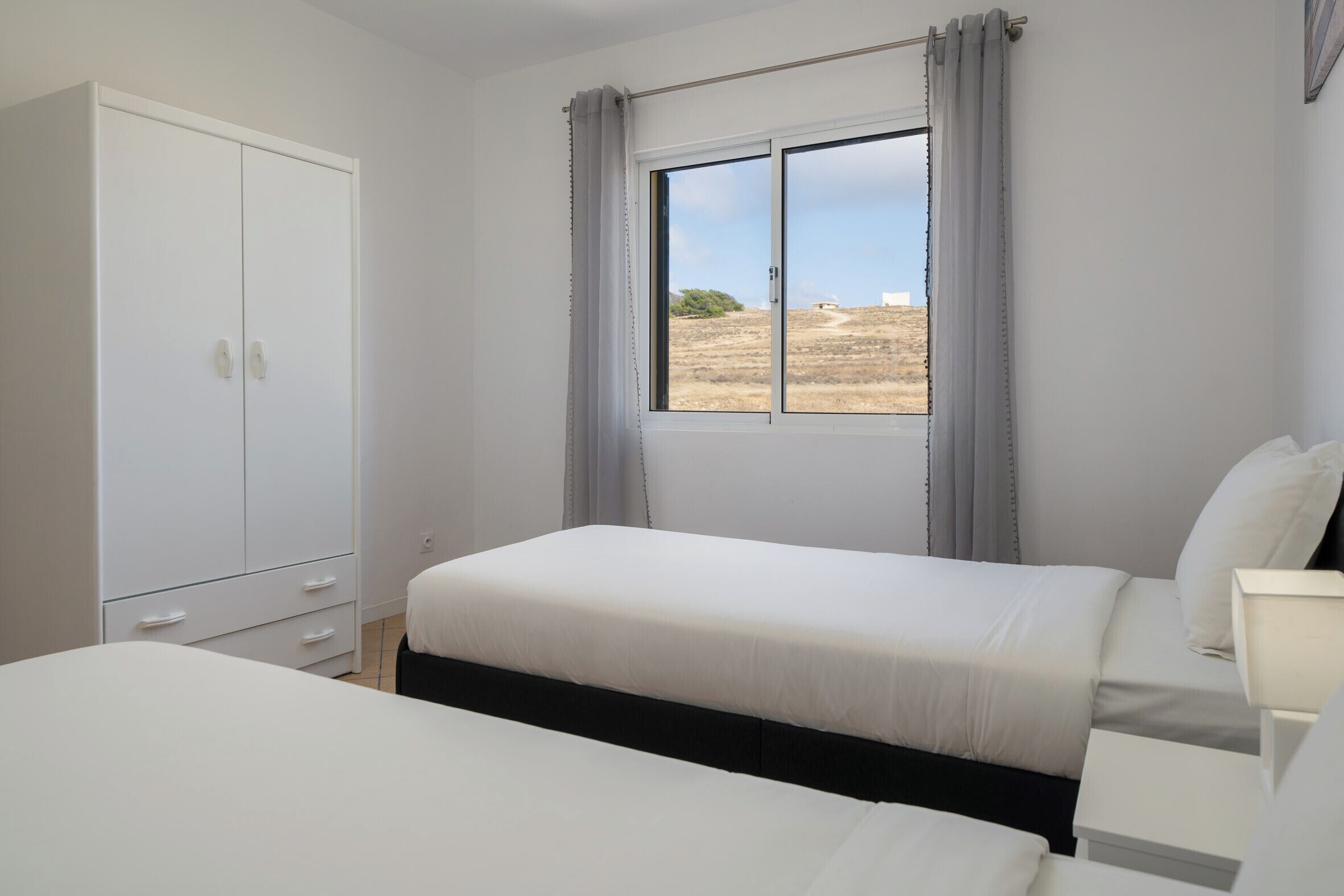 Ein Schlafzimmer mit einem Einzelbett, einem Nachttisch, einem Kleiderschrank und einem Fenster mit Vorhängen.