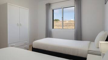 Ein Schlafzimmer mit einem Einzelbett, einem Nachttisch, einem Kleiderschrank und einem Fenster mit Vorhängen.