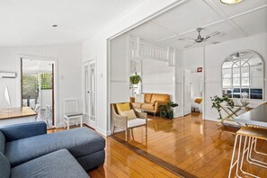 A spacious living area with a wooden floor, a blue sofa, a tan armchair, and a white chair. - Classic Queenslander - walk to suncorp (Milton)