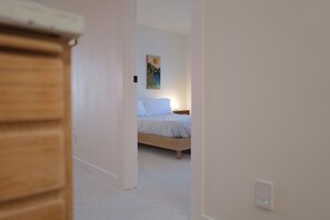 Une chambre à coucher comprenant un lit, une table de chevet, un tableau accroché au mur et une porte donnant sur une autre pièce.