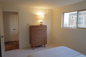 Un dormitorio con una cama, un aparador, una ventana y una puerta.