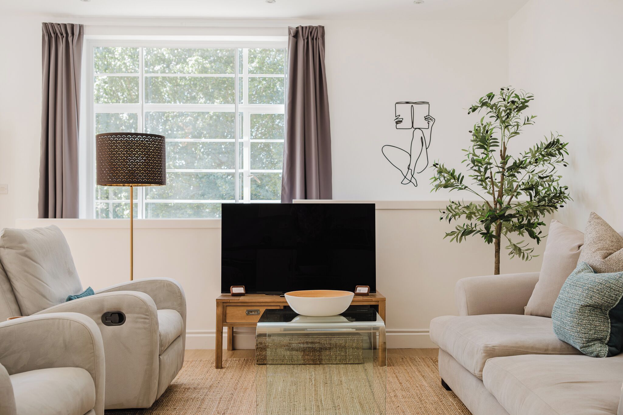 Ein Wohnzimmer mit einem Flachbildfernseher auf einem Holzboden, zwei Sofas, einer Stehlampe, einer Topfpflanze und einem Wandbild.
