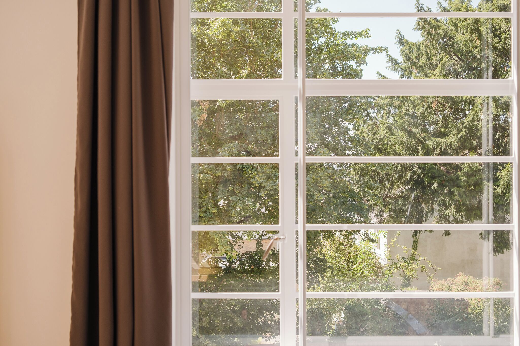 A window with multiple panes, a brown curtain, and a view of trees and buildings outside.