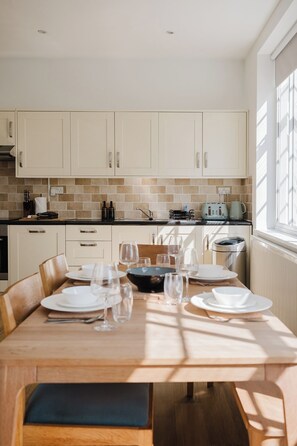 Una cocina moderna con armarios blancos, una encimera negra y una mesa de comedor preparada para seis comensales.