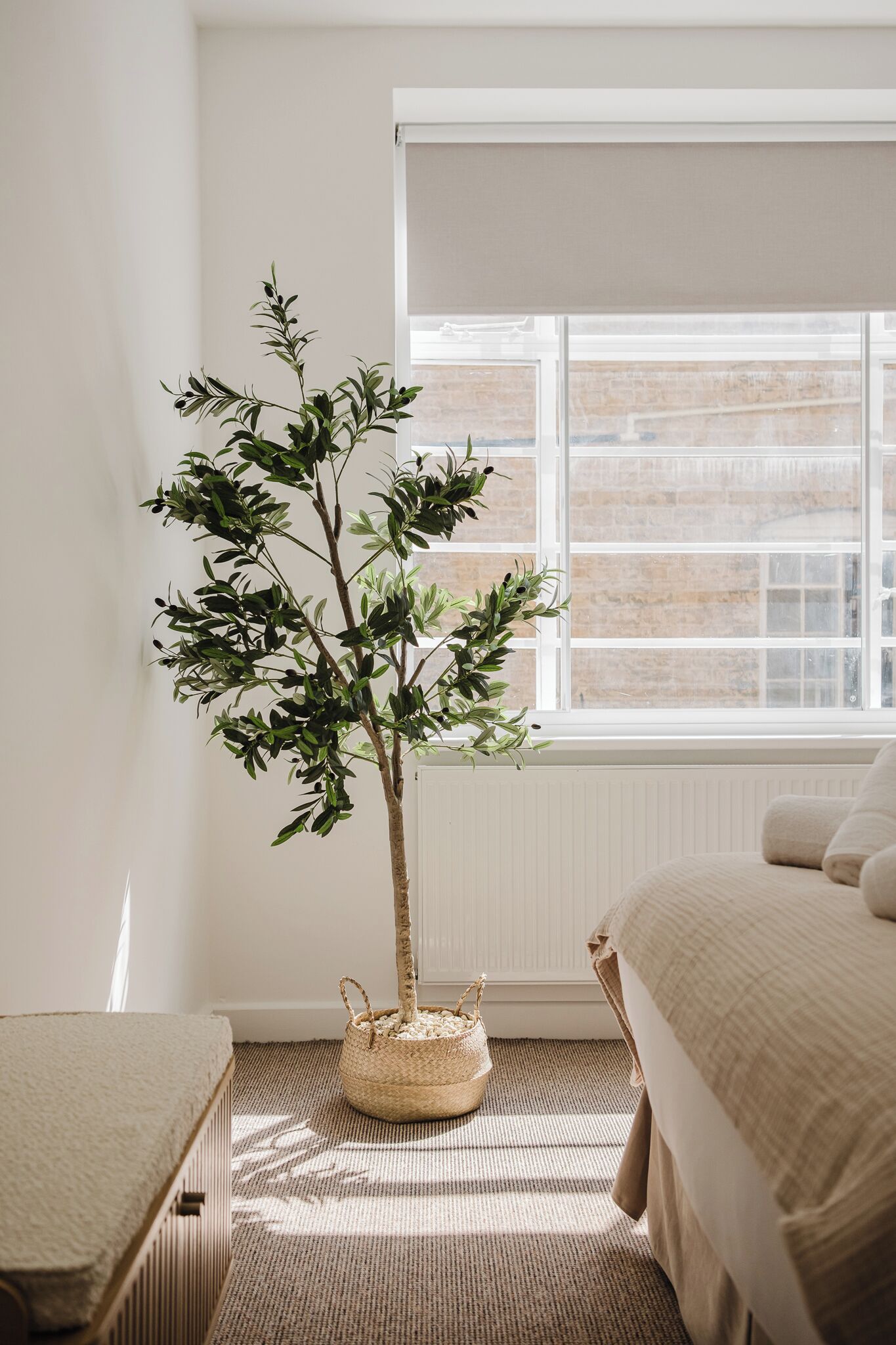Un dormitorio con un ventanal grande, una cama, una mesita y una planta en maceta.