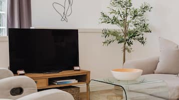 Un salon avec un téléviseur à écran plat posé sur un meuble en bois, un canapé, une table basse et un élément décoratif mural.