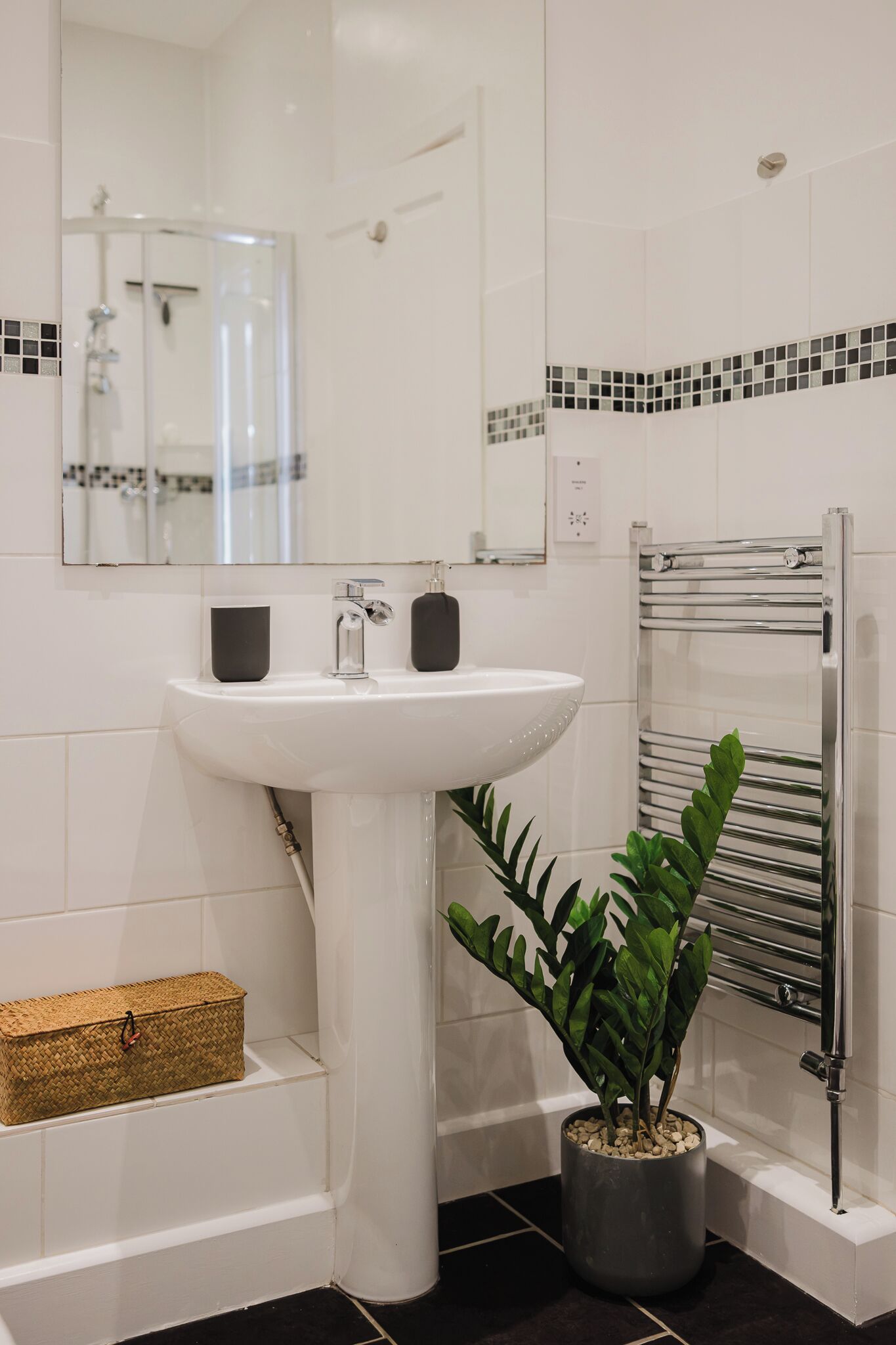Ein Badezimmer mit Waschbecken, Spiegel, Handtuchhalter und einer Topfpflanze.