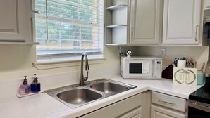 A kitchen with a double sink, a microwave, and a window with blinds.