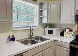 A kitchen with a double sink, a microwave, and a window with blinds.