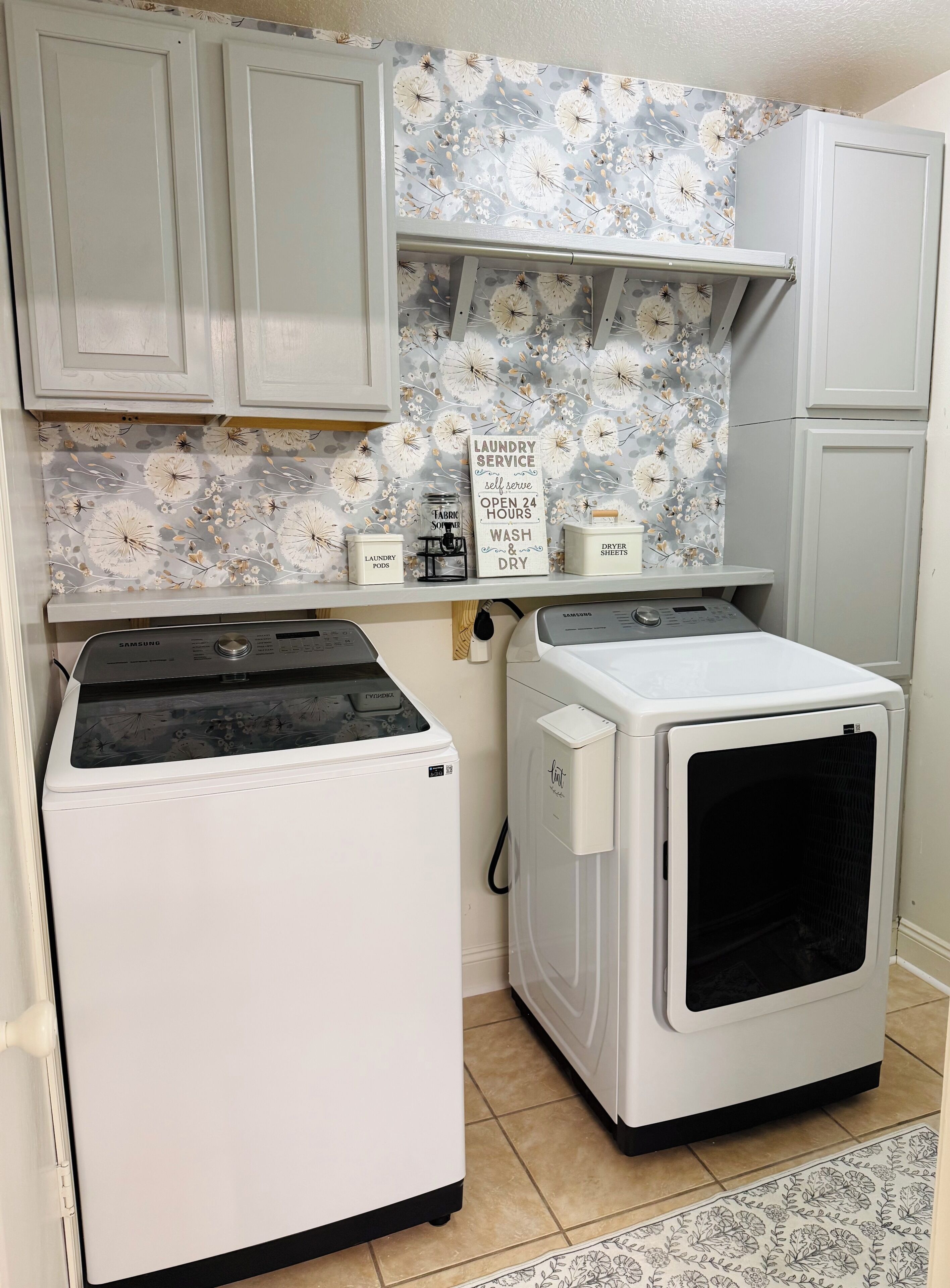 A laundry room with a Samsung washer and dryer, a shelf with laundry supplies, and a sign offering laundry service.