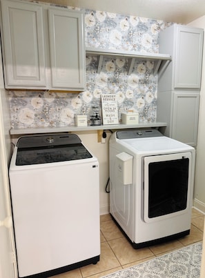 A laundry room with a Samsung washer and dryer, a shelf with laundry supplies, and a sign offering laundry service. - Southern Charm Near the Beach -- 3BR/2BA with Porch and Sunroom (Ocean Springs)