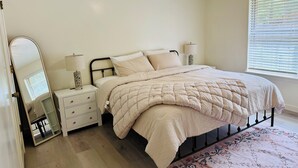 A bedroom with a bed, nightstands, a mirror, and a window with blinds.
