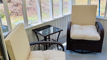 A covered patio area with wicker furniture and a glass-top table.