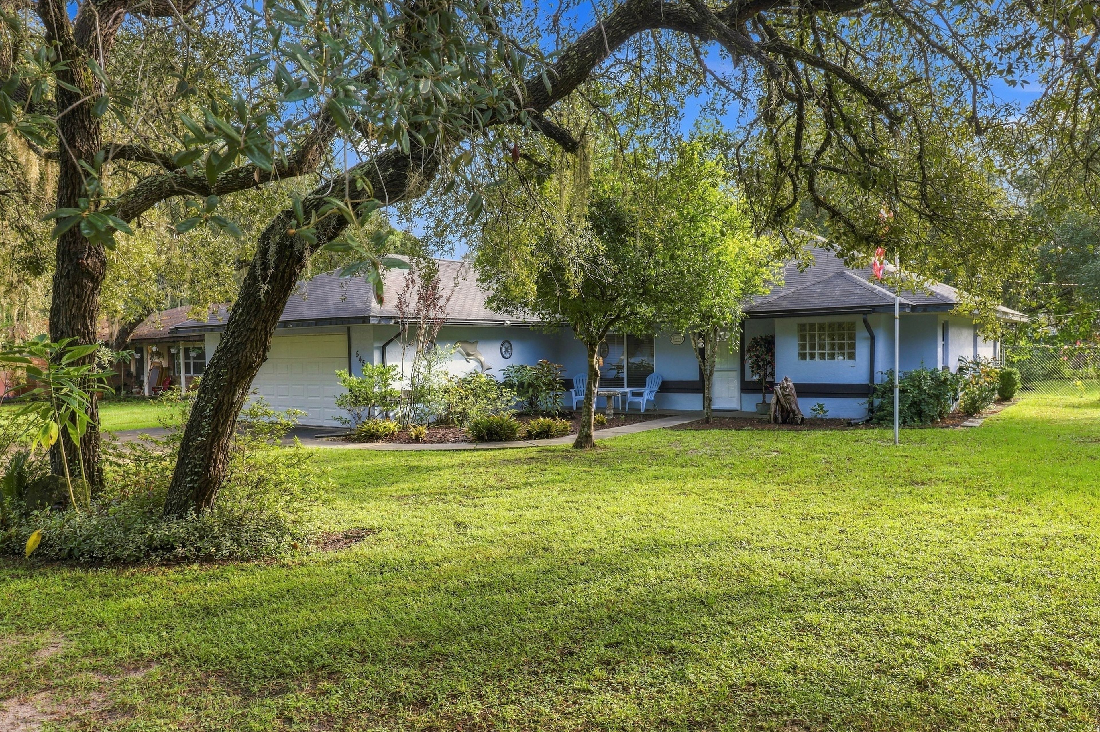 A residential house with a well-maintained lawn, a porch with outdoor seating, and a large tree in the foreground.