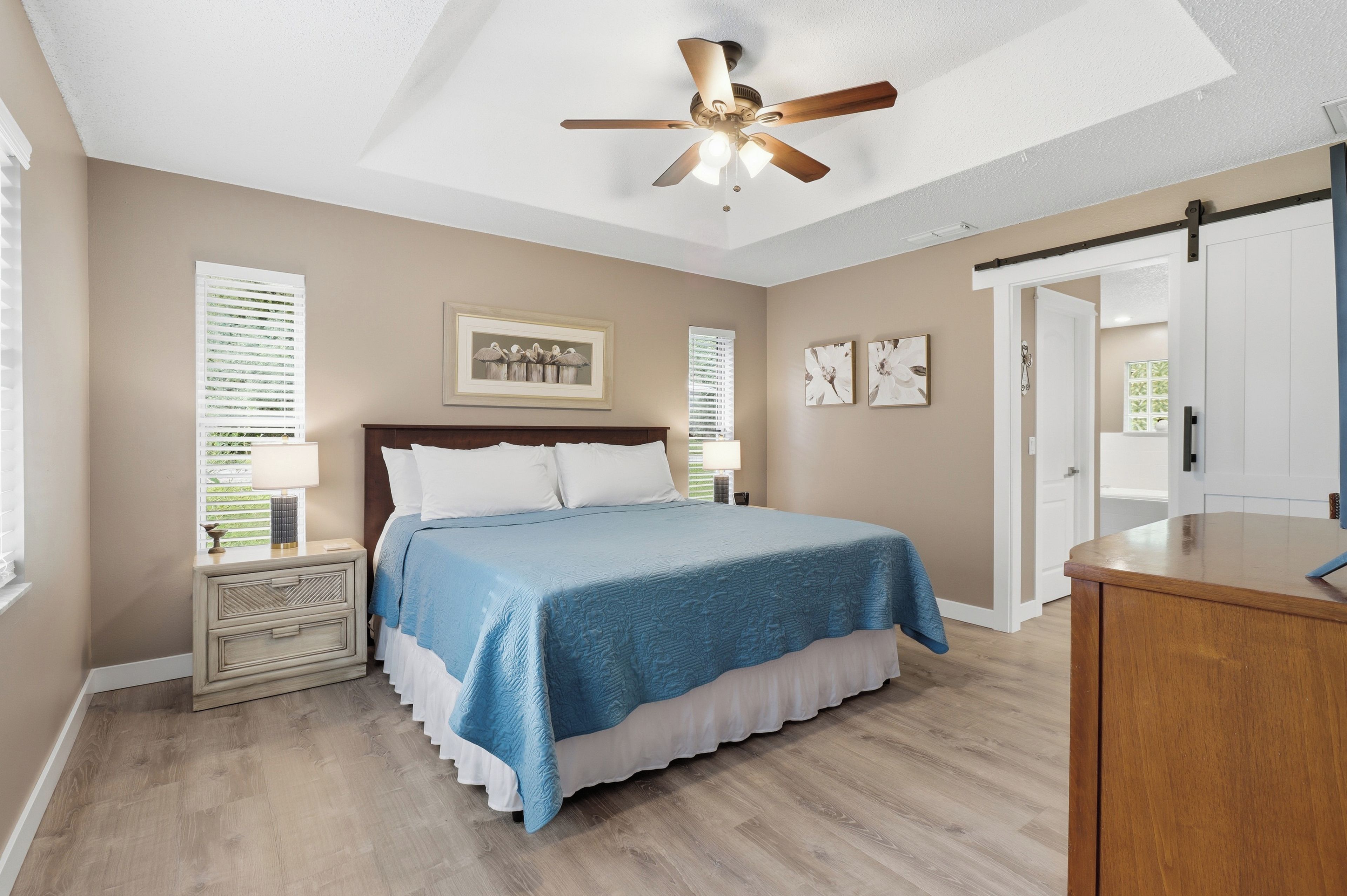 A bedroom with a bed, a ceiling fan, a nightstand, a dresser, and a door.