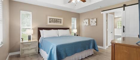 A bedroom with a bed, a ceiling fan, a nightstand, a dresser, and a door.