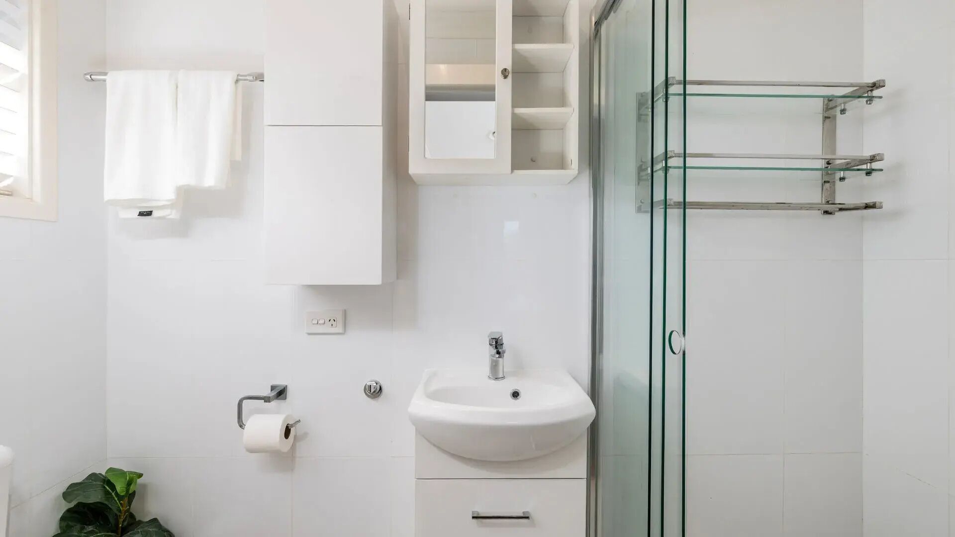 A modern bathroom with a glass shower enclosure, a white sink, and a toilet paper holder.