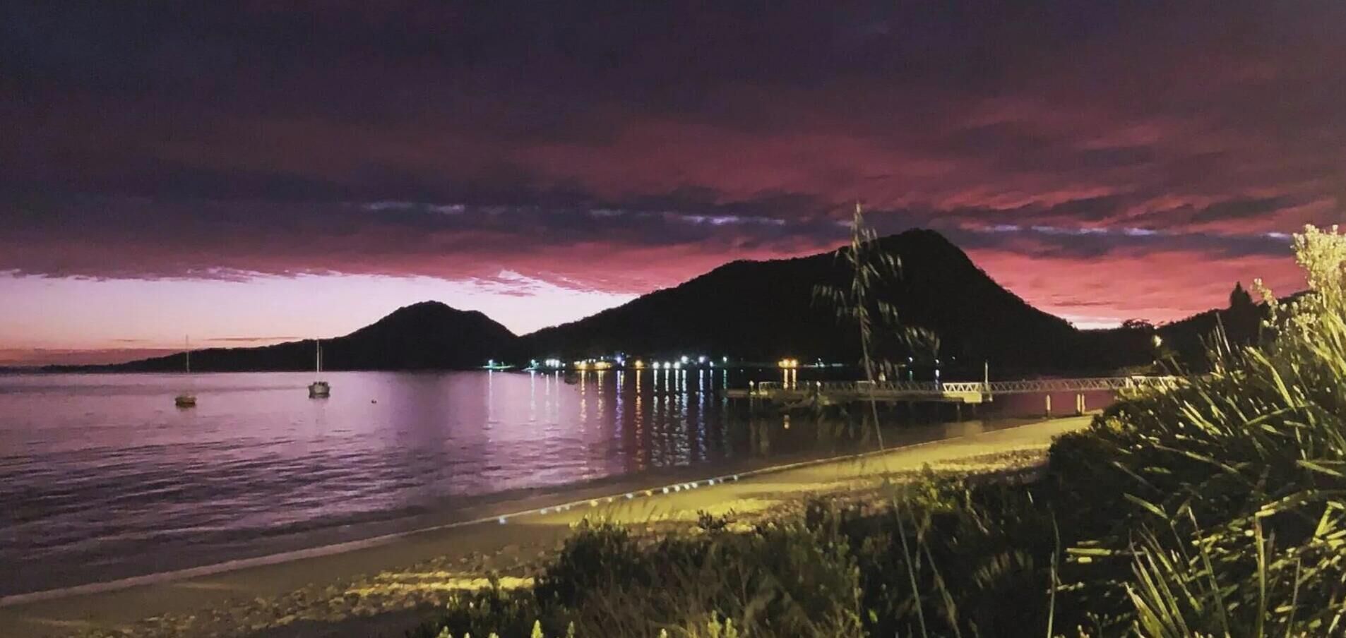 A waterfront scene with a mountain in the background, a bridge, and a body of water reflecting lights.