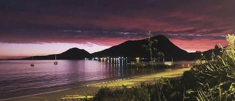 Escena costera con una montaña al fondo, un puente y un cuerpo de agua que refleja luces.