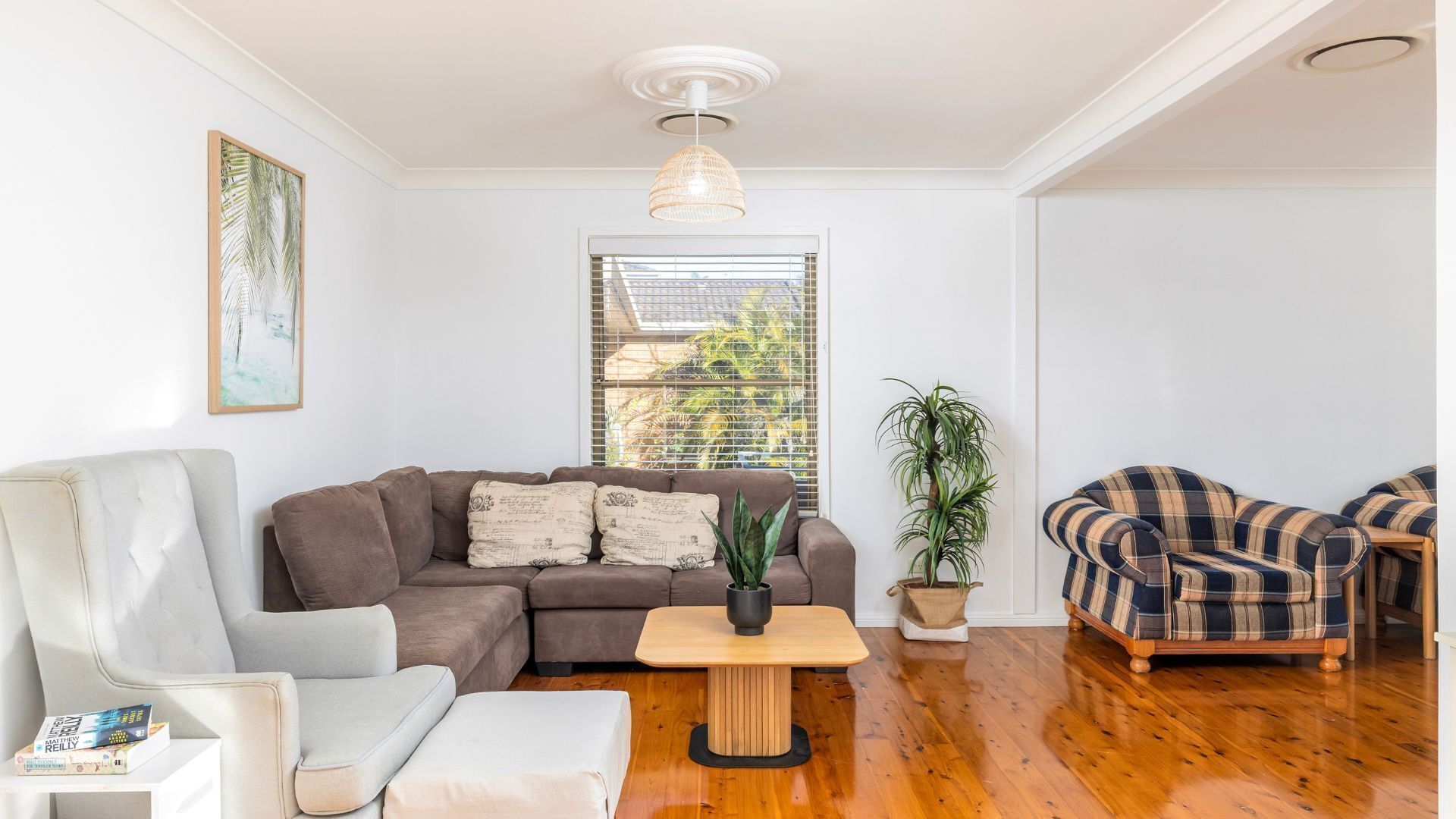 A living room with a brown sofa, a white armchair, a wooden coffee table, and a plaid sofa.