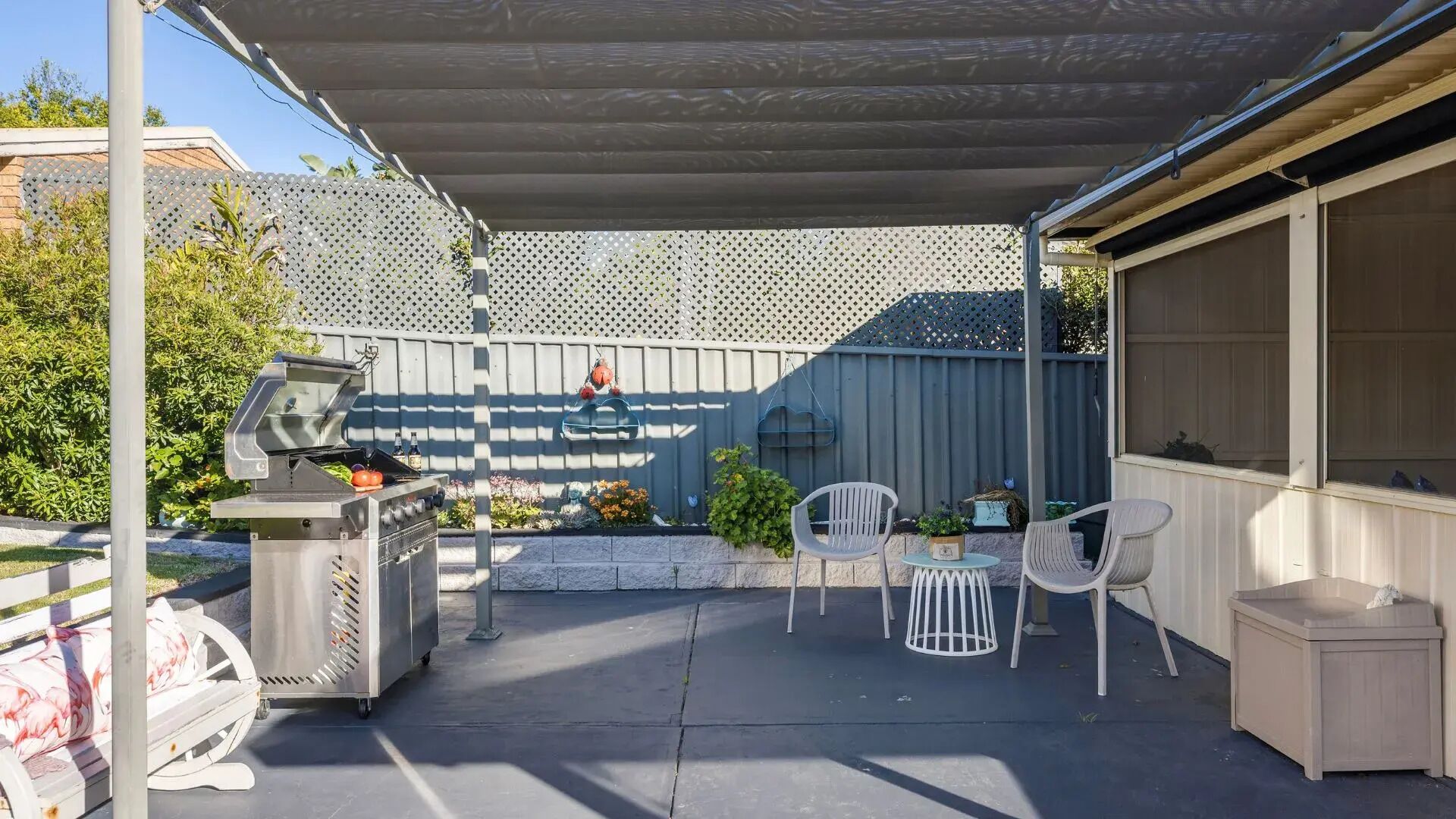 A covered patio area with a barbecue grill, outdoor seating, and a decorative fence.