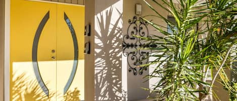 Una puerta amarilla de diseño peculiar, una pared decorativa con un patrón de metal y una planta verde en primer plano.