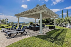 A covered outdoor seating area with lounge chairs and a pergola. - Spacious 5-bedroom in Temecula Wine Country w/Pool/Spa/Fire pit/View (Temecula)