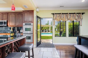 A kitchen with a built-in oven and microwave, a dining area with a bench, and a view of a pool through a glass door.
