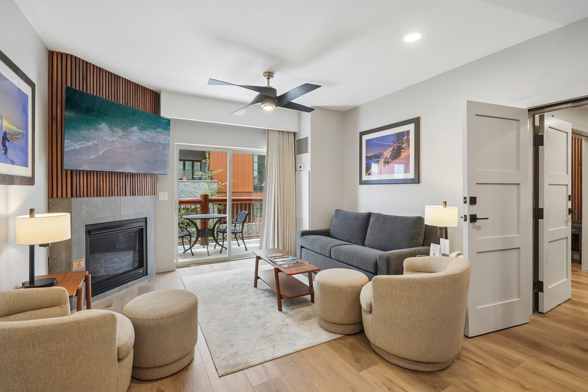 A modern living room with a fireplace, a ceiling fan, and a view to an outdoor balcony.