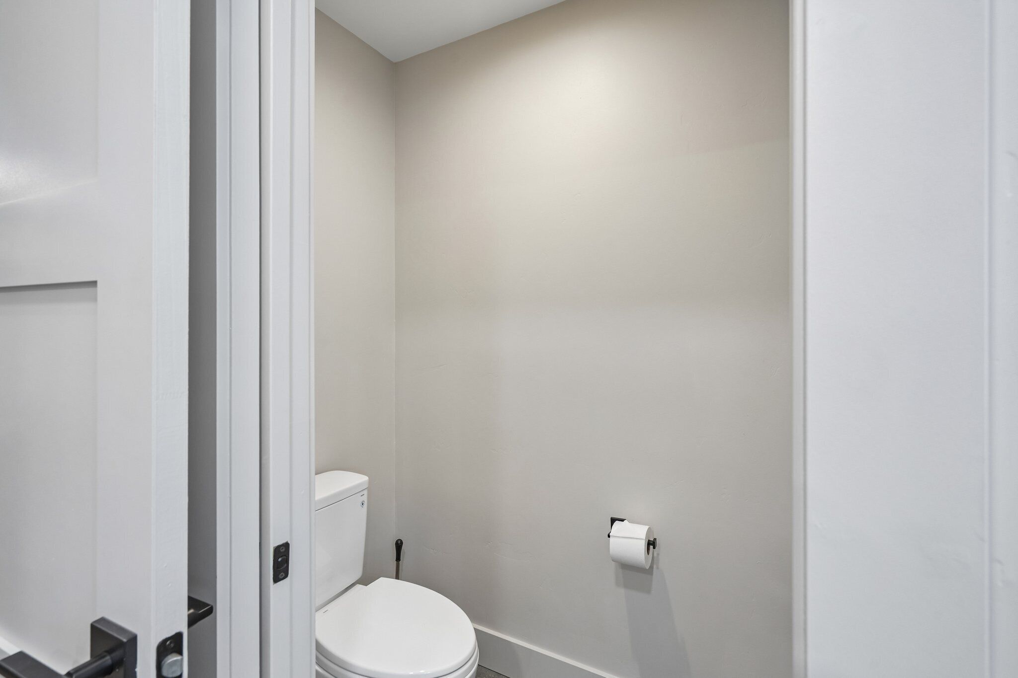 A small, clean bathroom with a toilet, a toilet paper holder, and a visible toilet paper roll.