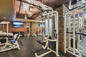 A gym with various exercise equipment, a television mounted on the wall, and a stone wall. - Luxury Westgate 2BR | Canyons Village | Pools, Spa & Ski Valet (Park City)