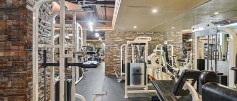 Un gimnasio con diverso equipo de ejercicio, una pared de piedra y una pared con espejos.