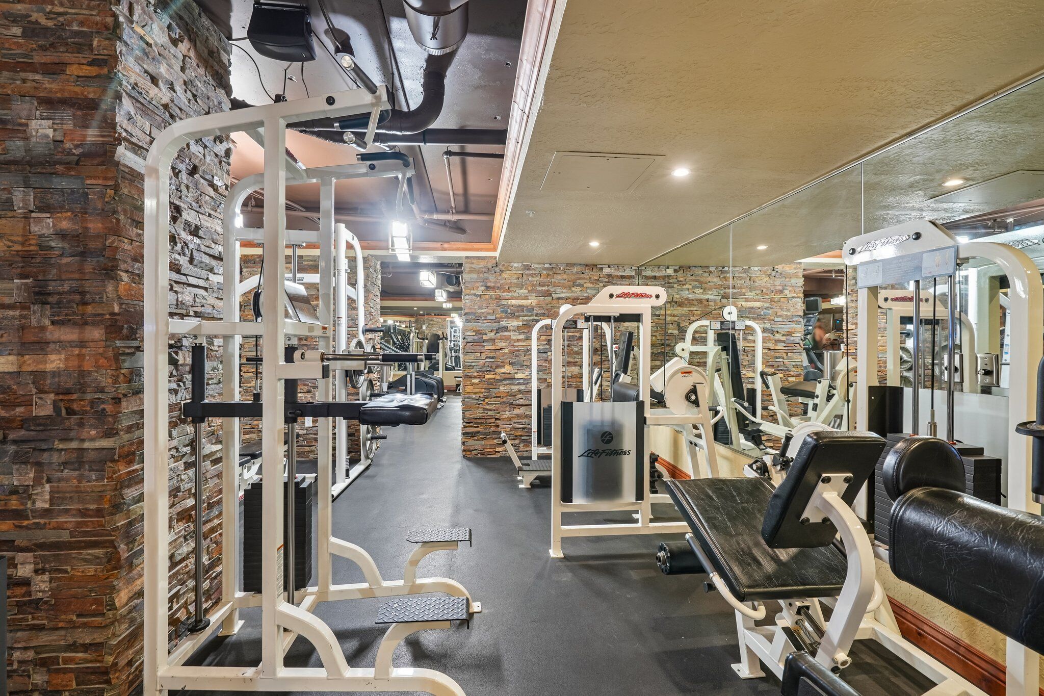 Une salle de sport équipée de divers appareils d’exercice, avec un mur en pierre et un mur recouvert de miroirs.