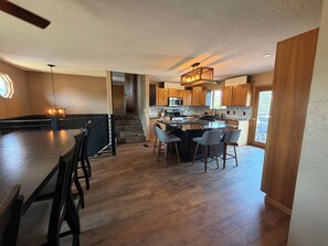 A spacious kitchen with a central island, wooden cabinets, and a staircase leading to an upper level.