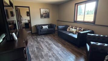 A living room with a wooden floor, two leather sofas, a coffee table, and a ceiling fan.