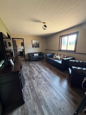 A living room with a wooden floor, two leather sofas, a coffee table, and a ceiling fan.
