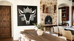 A dining area with a long wooden table, chairs, a stone fireplace, and a large black artwork on the wall. - Luxury Temecula Estate Pool Spa Views Theater (Temecula)