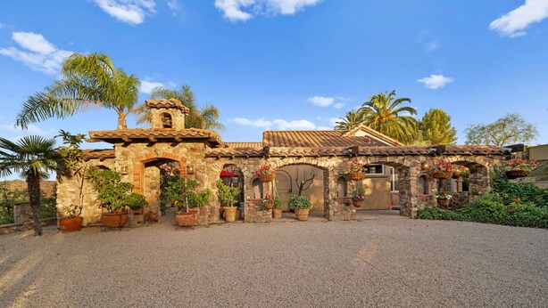 A courtyard with a stone archway, potted plants, and a building with a tiled roof. - Luxury Temecula Estate Pool Spa Views Theater (Temecula)